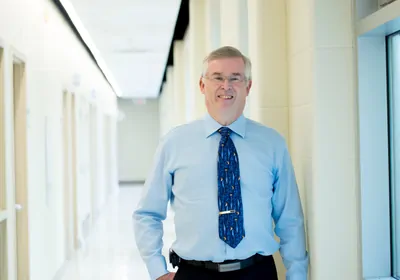 Man with blue shirt and tie smiling at camera.